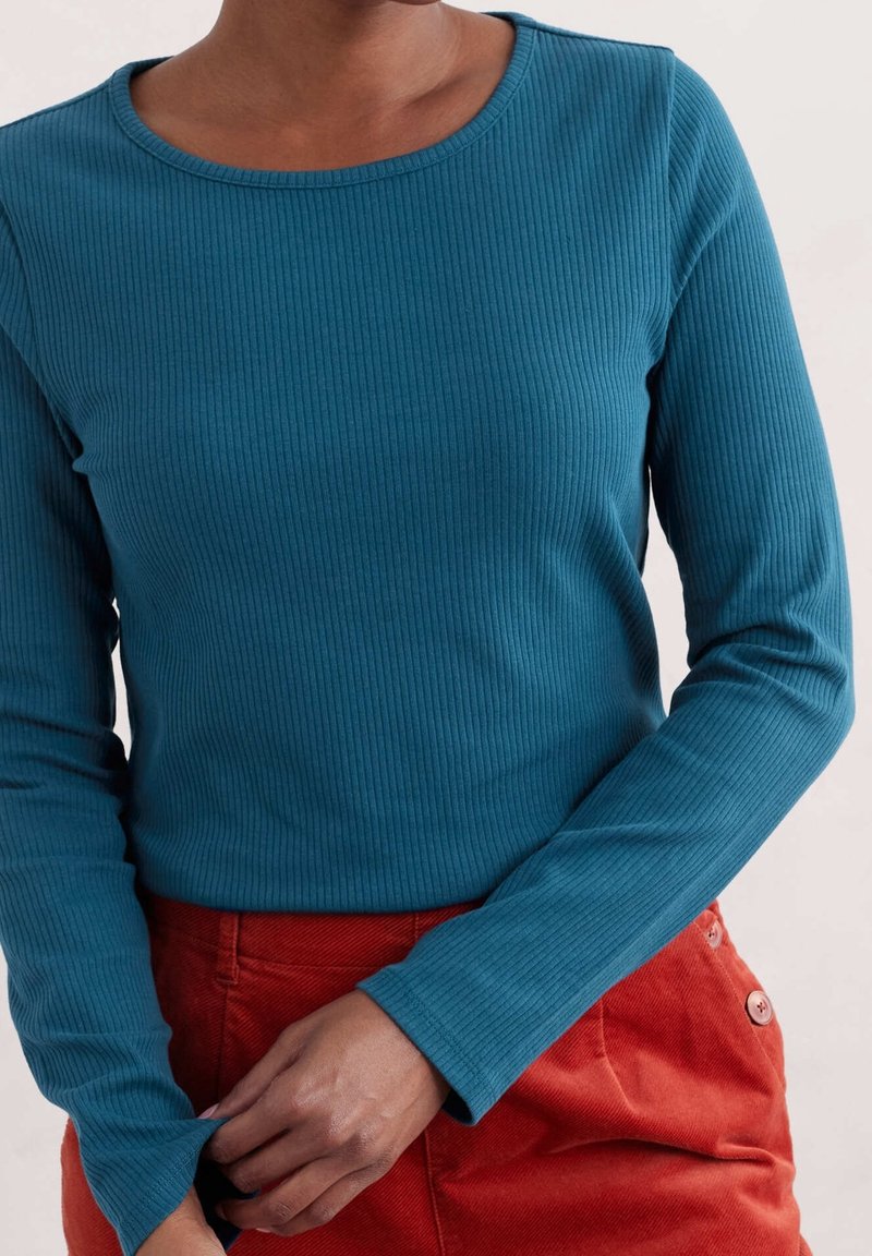 Geribbelde top met lange mouwen in teal, met een ronde halslijn en een aansluitend ontwerp, gecombineerd met rode ribfluwelen broek met knoopdetails.