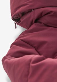 Burgundské polstrované přikrývka s hladkým povrchem a viditelným zipem. Měkký prošívaný design s bohatou barvou a odolnou tkaninou.