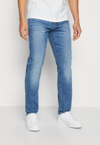 Light blue denim jeans with a straight leg design, featuring a five-pocket style and subtle fading. Worn with white sneakers.