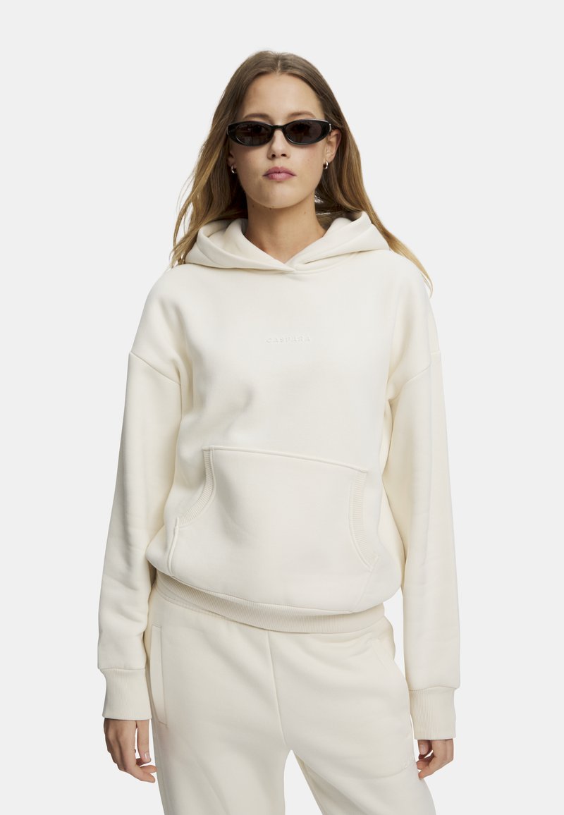 Krämfärgad hoodie med en framficka, vadderade ärmslut och fåll. Har en diskret logga på bröstet. Matchas med krämfärgade sweatpants.