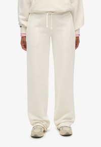 Svedbukser i cremefarve lavet af blødt stof med en afslappet pasform, der har snøre i taljen og sidelommer, kombineret med mønstrede sneakers.