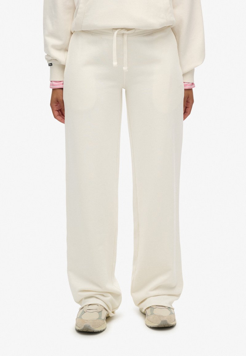 Svedbukser i cremefarve lavet af blødt stof med en afslappet pasform, der har snøre i taljen og sidelommer, kombineret med mønstrede sneakers.