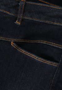 Jeans din denim închis au cusături portocalii, un buzunar frontal și o textură netedă. Materialul are un luciu subtil și un design clasic.