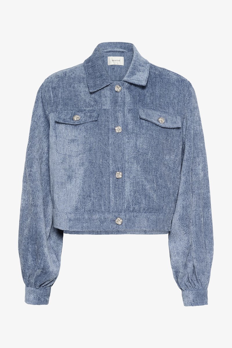 Veste courte en chevrons bleus avec manches longues bouffantes, deux poches poitrine et boutons argentés en accent. Tissu texturé avec un léger éclat.