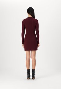 Vestido de malha canelada em burdeos com mangas longas e bainha em forma de escalope, combinado com botas de tornozelo pretas de salto alto. Design minimalista.