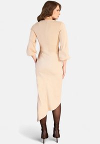 Abito midi beige con orlo asimmetrico, scollo rotondo e maniche a tre quarti, abbinato a stivaletti con tacco alto marroni.