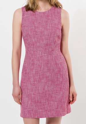 Robe texturée rose sans manches avec une taille cintrée portée par une personne sur un fond clair uni.