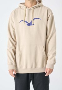 Felpa beige con tasca frontale, cappuccio regolabile con cordino e una grafica di un uccello viola sul petto. Materiale in cotone con una texture liscia.