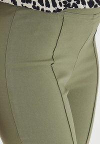 Pantalons ajustés vert olive avec une texture lisse, présentant des coutures contrastées le long des coutures et un design épuré.