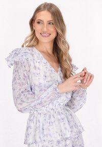 Gennemsigtig, lavendelfarvet bluse med blomsterprint, flæser på ærmerne, v-hals og elastisk talje. Letvægtsstof med blød, strømmende tekstur.