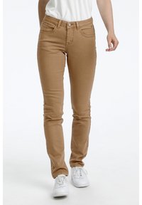 Bruna slim jeans gjorda av ett mjukt, stretchigt tyg med framfickor, bältesslingor och en ensam knappstängning. Bärs med vita sneakers.