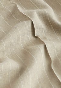 Beżowy materiał z teksturowanym splotem, z subtelnymi białymi paskami. Tkanina wydaje się miękka i gładko układa się, podkreślając swoje naturalne włókna.