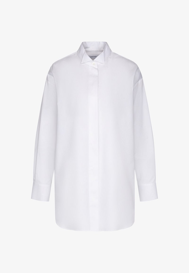 Chemise blanche oversize à manches longues avec patte de boutonnage dissimulée et col pointu, présentée sur un fond uni.