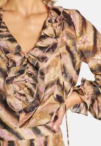 Blusa de manga larga con escote en V profundo, cuello con volantes y un patrón abstracto multicolor en tonos de rosa, marrón y dorado.