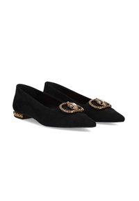 Zapatos planos de ante negro con punta afilada, adornados con una hebilla decorativa en tono dorado que presenta un detalle de piedra en cada zapato. Tacón plano.