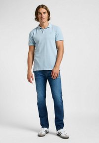 Ljusblå polo skjorta med korta ärmar, ribbad krage och slim fit, i kombination med mörk denim jeans och vita sneakers med svarta detaljer.