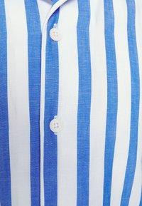 Camicetta a strisce blu e bianche realizzata in tessuto leggero, con chiusura a bottoni e un design classico del colletto, che enfatizza le strisce orizzontali.