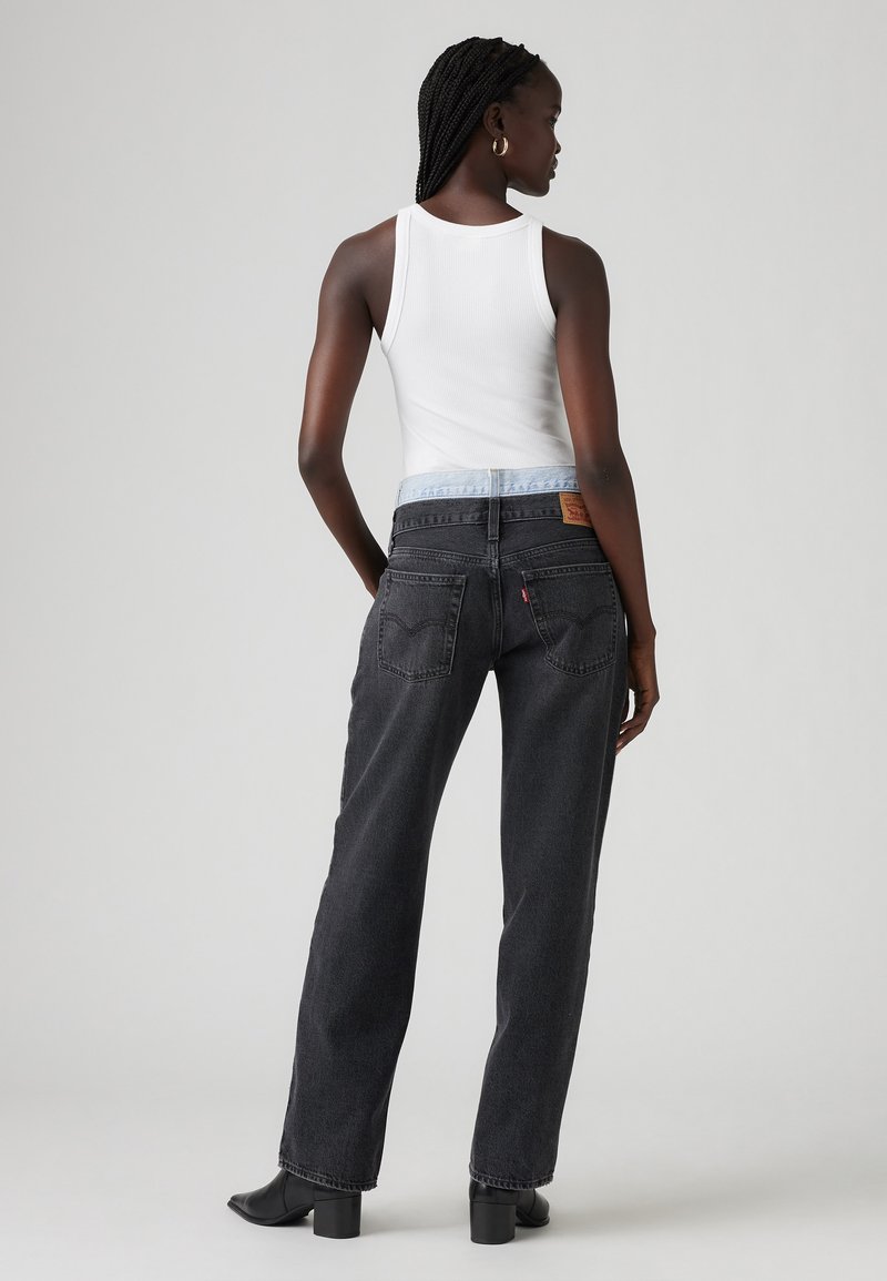 Jeans noirs à coupe droite avec une taille en denim bleu clair, comportant cinq poches et un patch en cuir au dos. Associés à un débardeur blanc.
