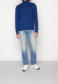 Suéter de cuello alto azul en tejido suave, combinado con jeans deslavados de un azul claro y zapatillas deportivas blancas. Diseño sencillo y silueta ajustada.