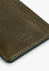 Billetera de cuero marrón con una textura suave, logo grabado, costuras en contraste y un diseño rectangular y elegante.