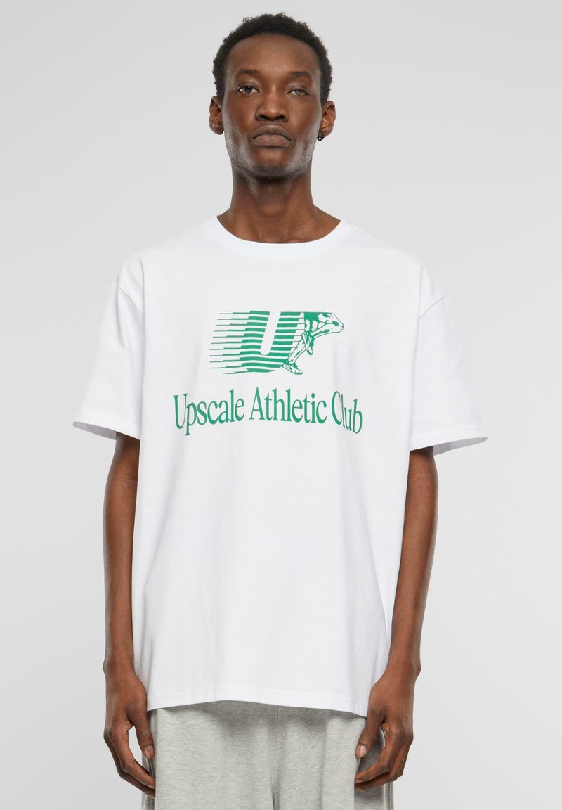 Balta medvilninė marškinėliai trumpomis rankovėmis su laisvu pjūviu. Pabrėžia žalią grafiškai atvaizduotą tekstą "Upscale Athletic Club" ir logotipą.