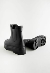 Bottes de cheville noires imperméables en caoutchouc texturé, à bout rond, à tige haute et à semelle épaisse à crampons. Présentent des accents moulés et une finition mate.