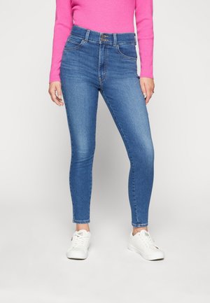 Jean skinny taille haute en denim bleu, avec une fermeture à boutons, cinq poches et une coupe ajustée jusqu'aux chevilles.