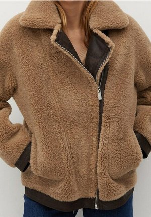 Brown teddy fleece jacket with large collar and visible silver zipper, worn over dark inner layer and blue jeans.