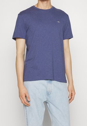 Męski t-shirt z krótkim rękawem i okrągłym dekoltem w melanżowym, ciemnoniebieskim bawełnianym materiale. Subtelne logo na piersi, luźny fason, zestawiony z jasnymi jeansami.