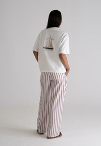 White short-sleeve shirt with a sailboat graphic on the back. Paired with wide-leg striped pants in light cream and burgundy.