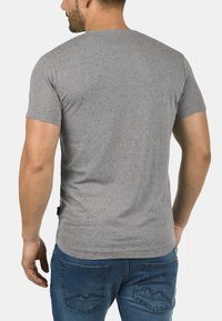 Grå kortærmet t-shirt med en spraglet tekstur, rund halsudskæring og en afslappet pasform; vist fra ryggen, parret med mørkeblå jeans.