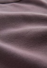 Zbliżenie na fakturę prążkowanej tkaniny w kolorze wrzosowym z miękkimi fałdami i delikatnymi pionowymi liniami dzianiny.