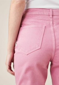 Pantalons en denim rose présentant un design ajusté, des poches arrière de forme pointue et un tissu lisse légèrement texturé.