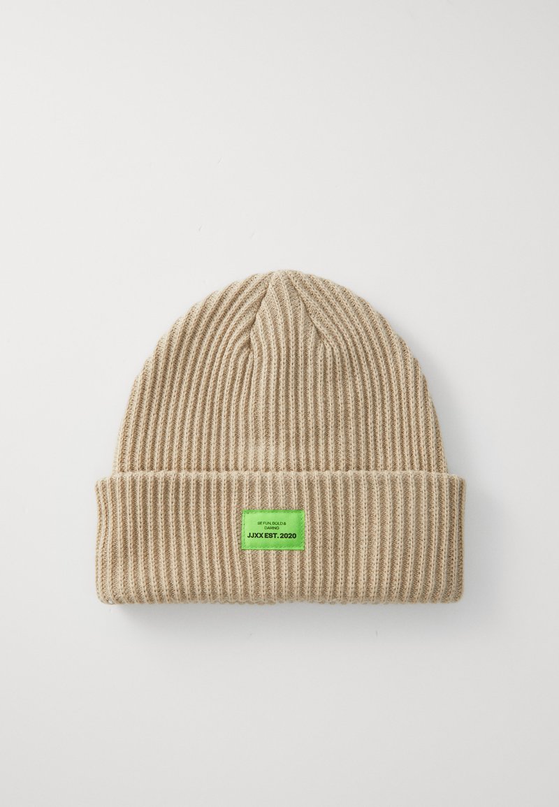 Beige ribbed knit beanie with a folded cuff and a green tag stating "JJXX EST. 2020." Textured fabric, warm and snug fit.