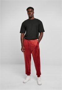 Black short-sleeve t-shirt with relaxed fit paired with red velvet joggers featuring an elastic waistband, side pockets, and white sneakers.