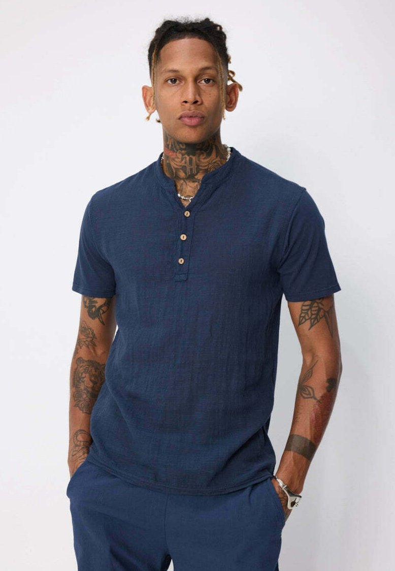 Chemise Henley à manches courtes bleu marine avec un tissu texturé, un col mandarin et une patte de boutonnage comportant quatre boutons marron.