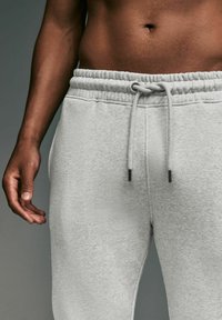 Lys grå sweatpants lavet af blødt stof, med en elastisk talje med snor og sidelommer. Tekstureret overfladedetalje.