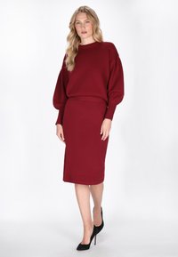 Burgunderfarbene Strickkleid-Set mit einem Langarmoberteil und einem knielangen Bleistiftrock. Mit gerippten Bündchen und einem taillierten Bund. Schwarze High Heels.