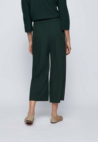 Mörkgröna, vida cropped-byxor med veck framtill. Mjuk, slät tyg och hög midja. Bärs med ljusbeiga slip-on skor.