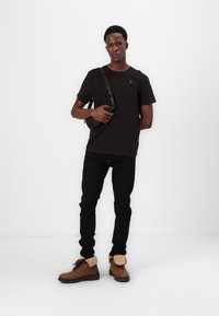 T-shirt noir à manches courtes, coupe décontractée, associé à un jean skinny noir. Bottes marron avec un col en fausse fourrure et un petit sac bandoulière noir.