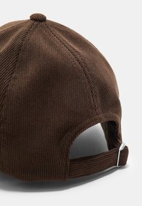 Hnedý kordový klobúk s okrúhlym dizajnom, štruktúrovaným povrchom a nastaviteľným pásikom s kovovými komponentmi na zadnej strane.