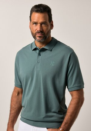 Polo shirt corto di colore verde scuro con maniche corte, colletto a tre bottoni, logo ricamato e una finitura in tessuto morbido e testurizzato.
