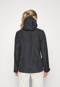 Giacca nera impermeabile con cappuccio, caratterizzata da una texture liscia, maniche lunghe e polsini regolabili. Design minimalista senza loghi visibili.