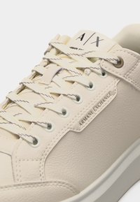 Baskets Armani Exchange couleur crème en cuir texturé, avec étiquette en métal de la marque, détails cousus et lacets blancs à motifs subtils.