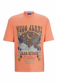 Camiseta de manga corta naranja, hecha de algodón, con un diseño gráfico que presenta flores, olas y el texto "FREE SPIRITS" en letras negritas.