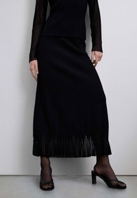 Conjunto de dos piezas de punto acanalado negro que incluye un top de manga larga y una falda larga hasta el suelo con dobladillo plisado, combinado con sandalias de tacón con tiras.