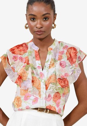 Blomsterbluse i gennemsigtigt hvidt stof med orange, pink og lilla blomstermønstre. Rynkede ærmer og knaplukning foran.