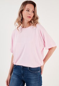 Světle růžové oversized tričko vyrobené z měkké látky, s kulatým výstřihem a krátkými rukávy, kombinované s tmavě modrými džíny.