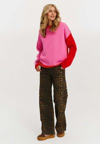 Różowy i czerwony sweter w dwa kolory z długimi rękawami, zestawiony z szerokimi spodniami w panterkę i brązowymi sandałami na platformie.