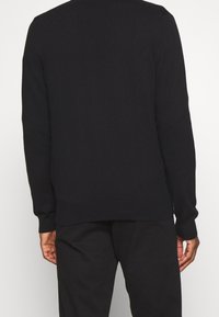 Pull en maille noire avec un col rond, des manches longues et des poignets côtelés. Texture lisse avec des fentes latérales à l'ourlet pour plus de confort.